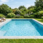 Piscine creusée neuve 8x4m dans jardin paysager, eau bleue scintillante, reflets du soleil.