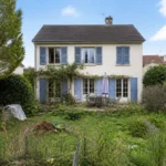 Maison à vendre avec jardin négligé, pelouse haute, terrasse encombrée et façade nécessitant une préparation avant vente